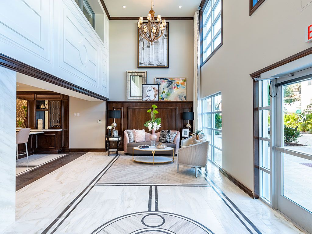 A luxurious living room with high ceilings, a central chandelier, and modern furnishings bathed in natural light.