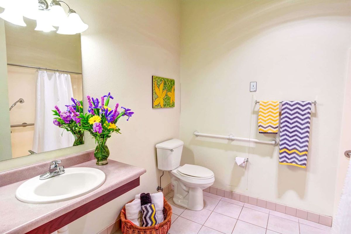 A bright and clean bathroom with colorful decor, featuring a toilet, sink with fresh flowers, and neatly arranged towels.