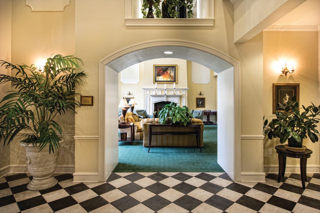 A cozy lobby area featuring comfortable seating, a fireplace, and lush plants under an elegant archway.