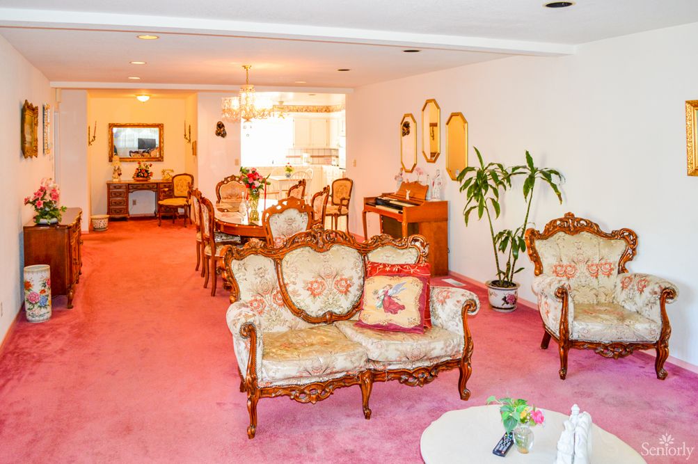 A spacious living and dining area featuring vintage furniture with a pink carpet and elegant decor.