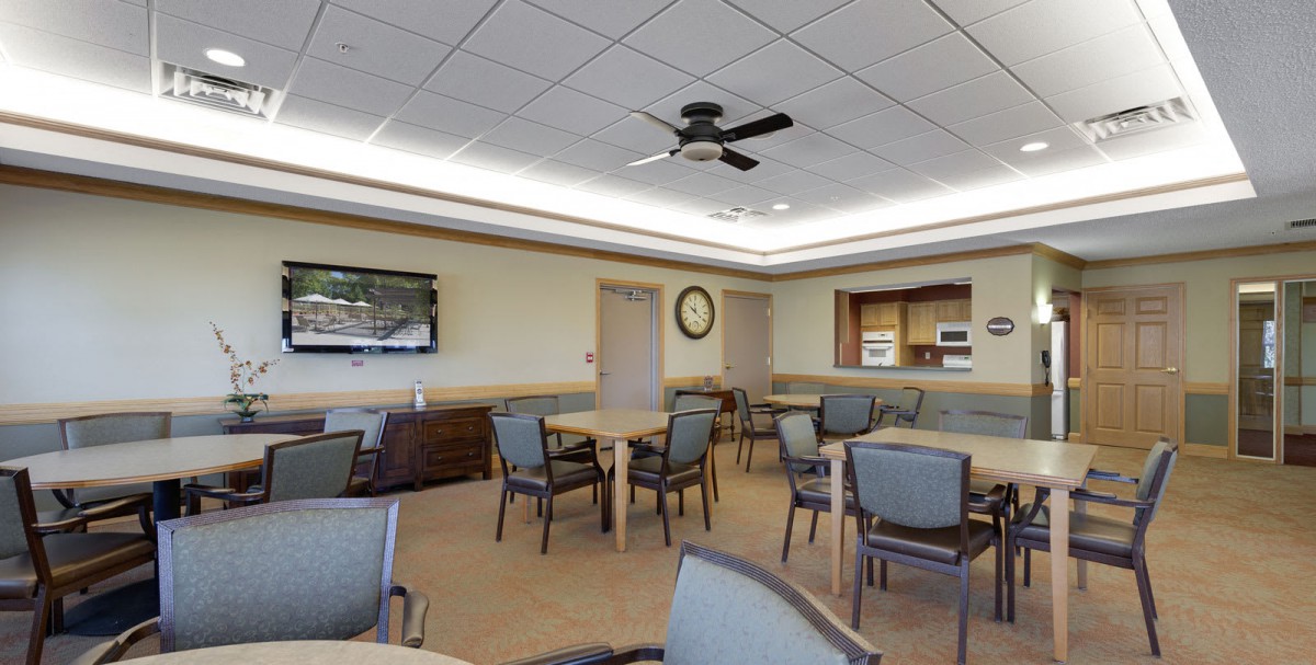A spacious dining room with tables and chairs, featuring a television, ceiling fan, and wall clock.