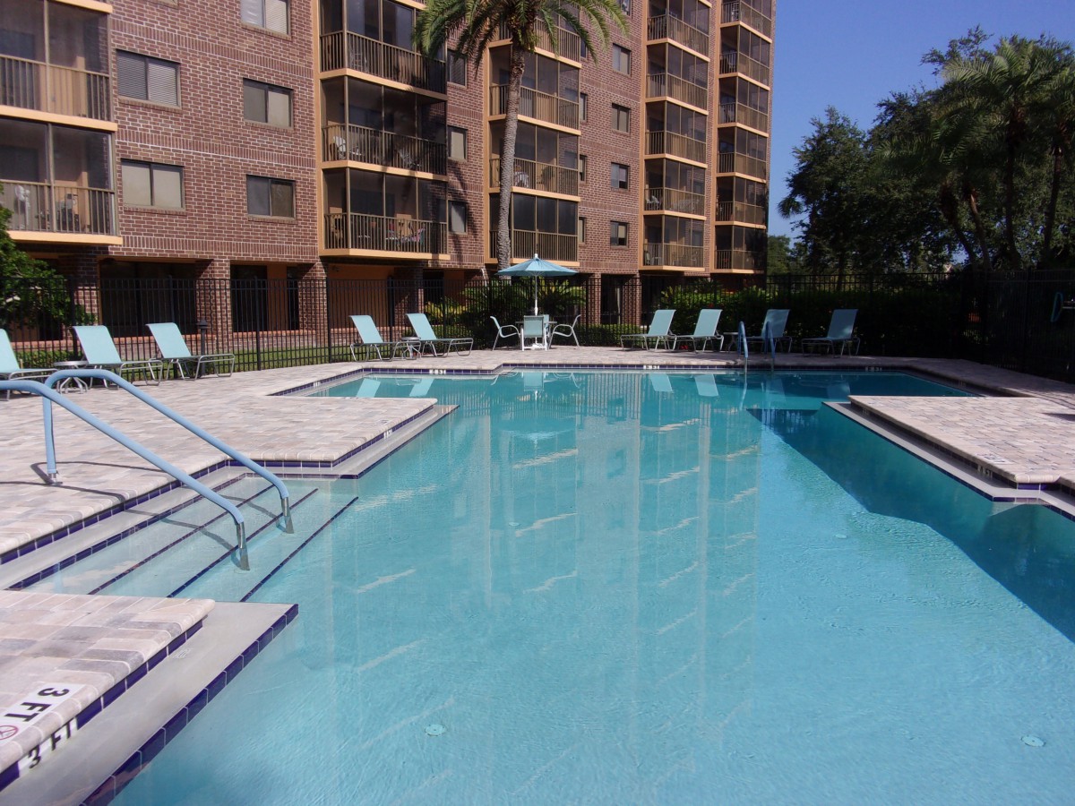 A relaxing outdoor swimming pool area next to an apartment building, surrounded by lounge chairs and palm trees.