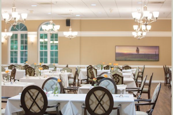 An elegant dining room with neatly arranged tables and chairs, adorned with chandeliers.
