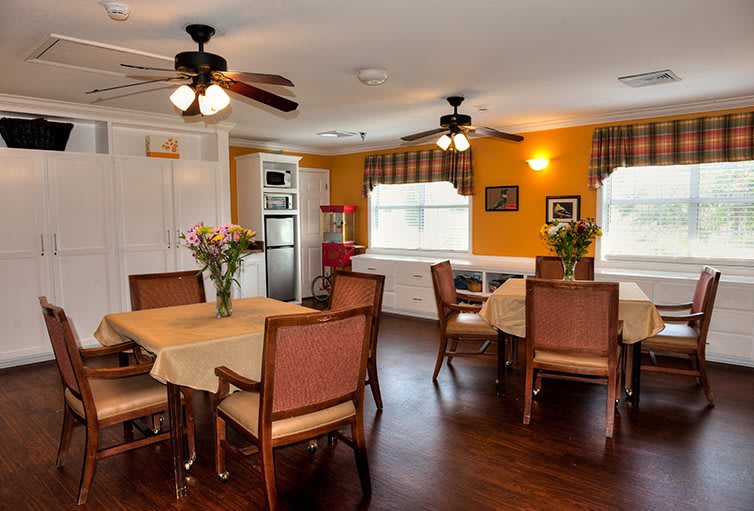 A cozy dining room with tables and chairs, adorned with vases of flowers and lit by ceiling fans.