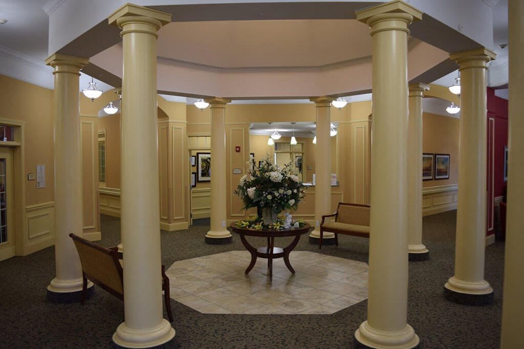 A well-lit lobby area featuring elegant columns and a central table with floral arrangements.