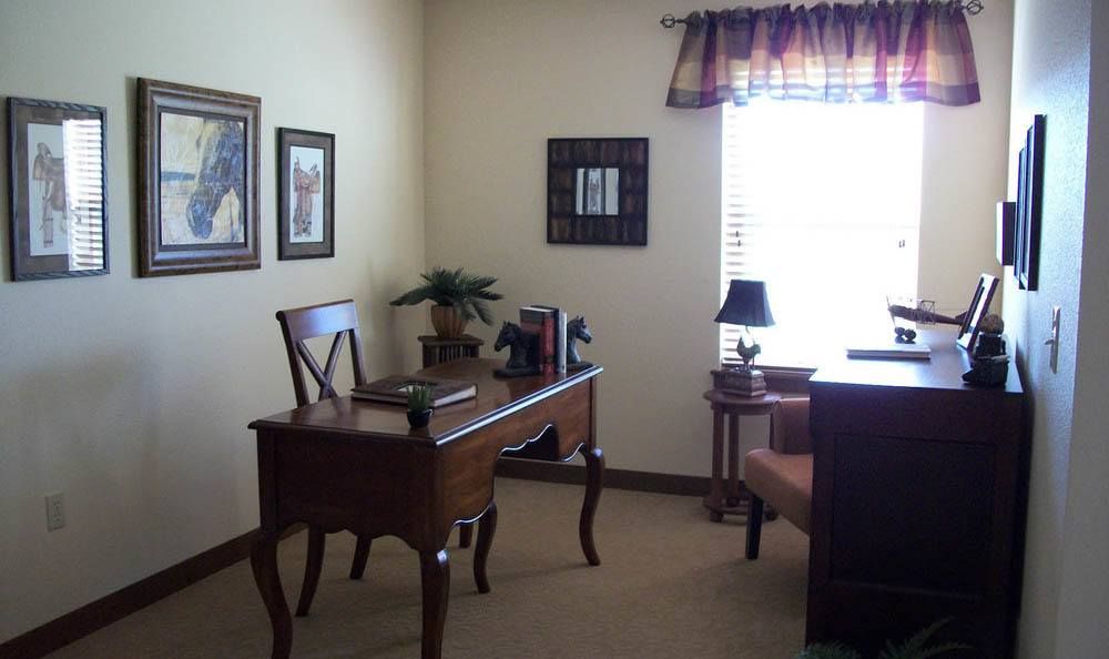 A small, neatly arranged office space with a wooden desk and chair, adorned with books and decorative elements near a window that lets in natural light.