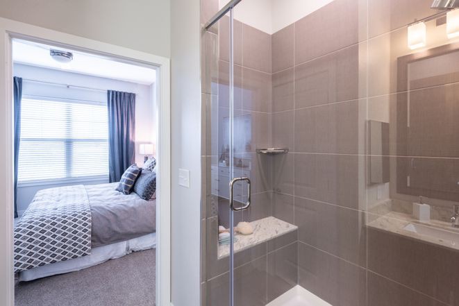 Modern bathroom with a glass shower next to a cozy bedroom.
