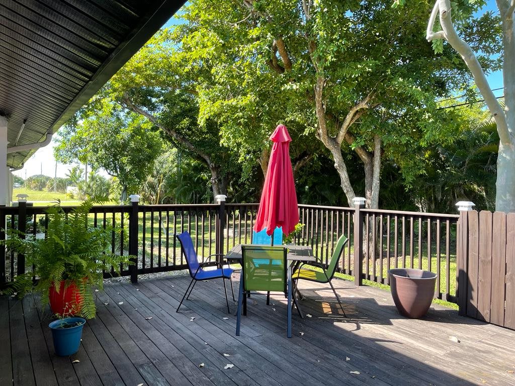 A peaceful outdoor deck with a table, chairs, and a red umbrella surrounded by trees.