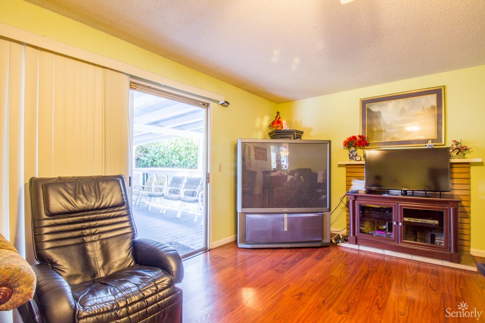 A cozy living room featuring a large television, leather chair, and fireplace, with hardwood flooring and a sliding glass door leading outside.