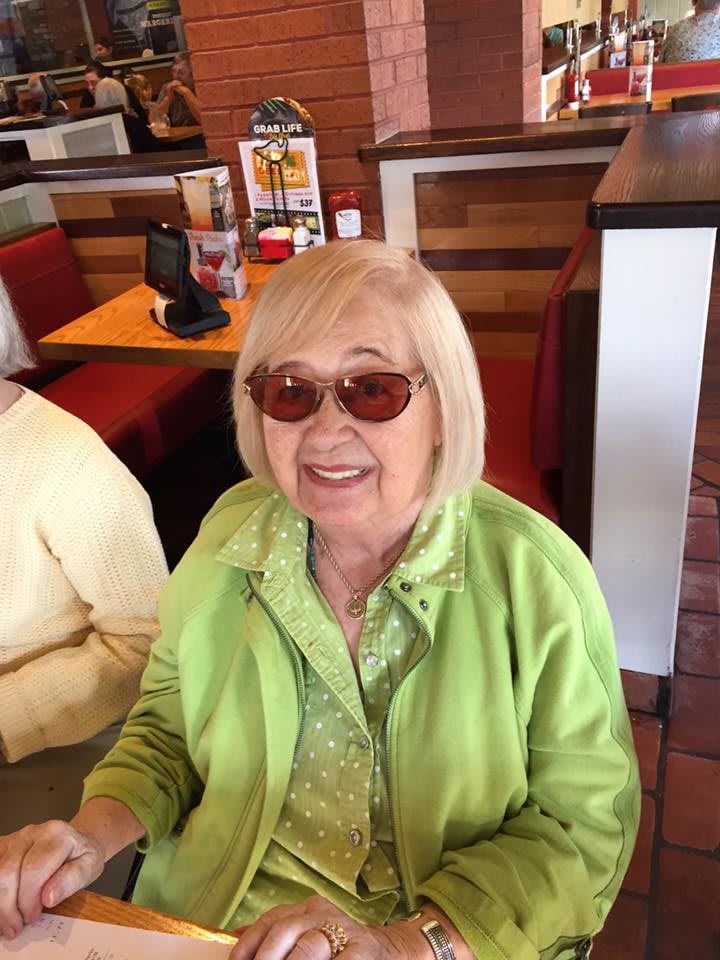 A smiling woman wearing glasses and a green outfit sits in a restaurant.