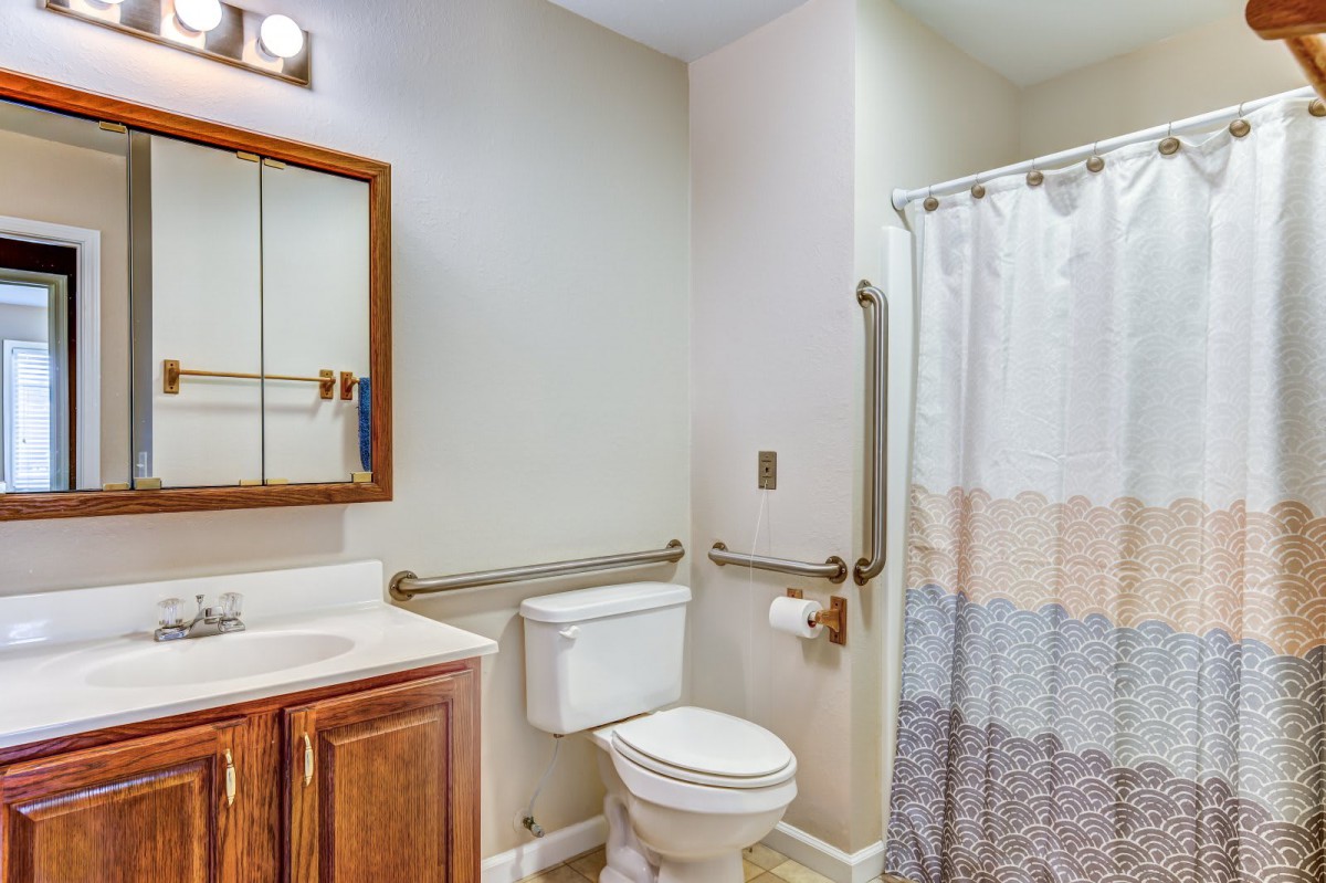 A bathroom with a toilet, shower curtain, sink, and safety grab bars.