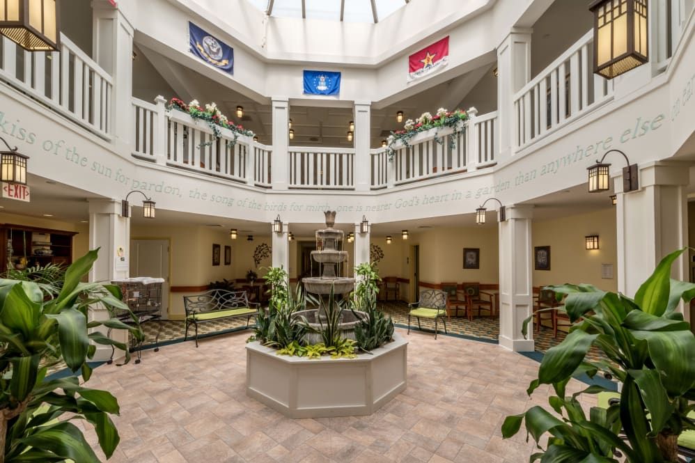 A bright atrium with a central fountain, surrounded by balconies and adorned with flags and plants.