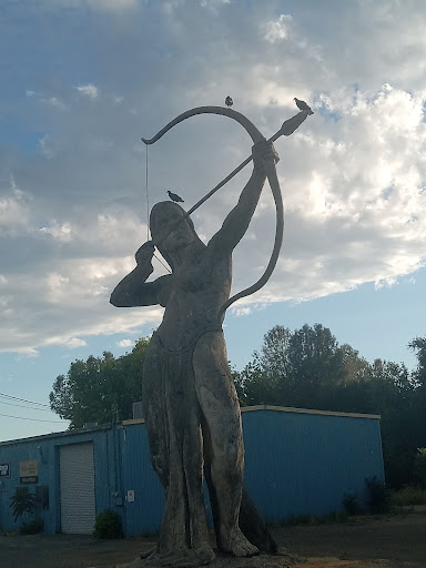 A striking statue of an archer poised with a bow, set against a beautiful cloudy sky.