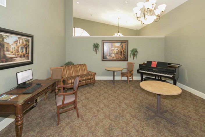 A cozy room with a piano, sofa, tables, and chairs under a chandelier.