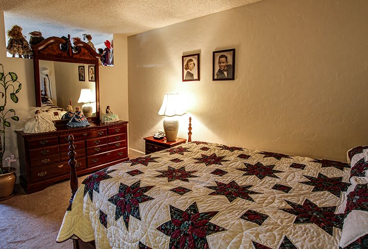A cozy bedroom with a star-patterned quilt on the bed and warm lighting from a bedside lamp, adorned with family photographs and wooden furniture.