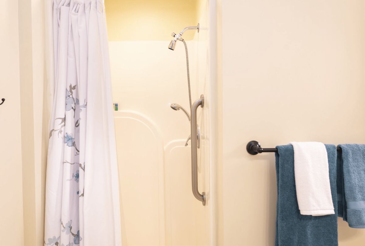 A bathroom featuring a walk-in shower with a grab bar, accompanied by a shower curtain and towels.