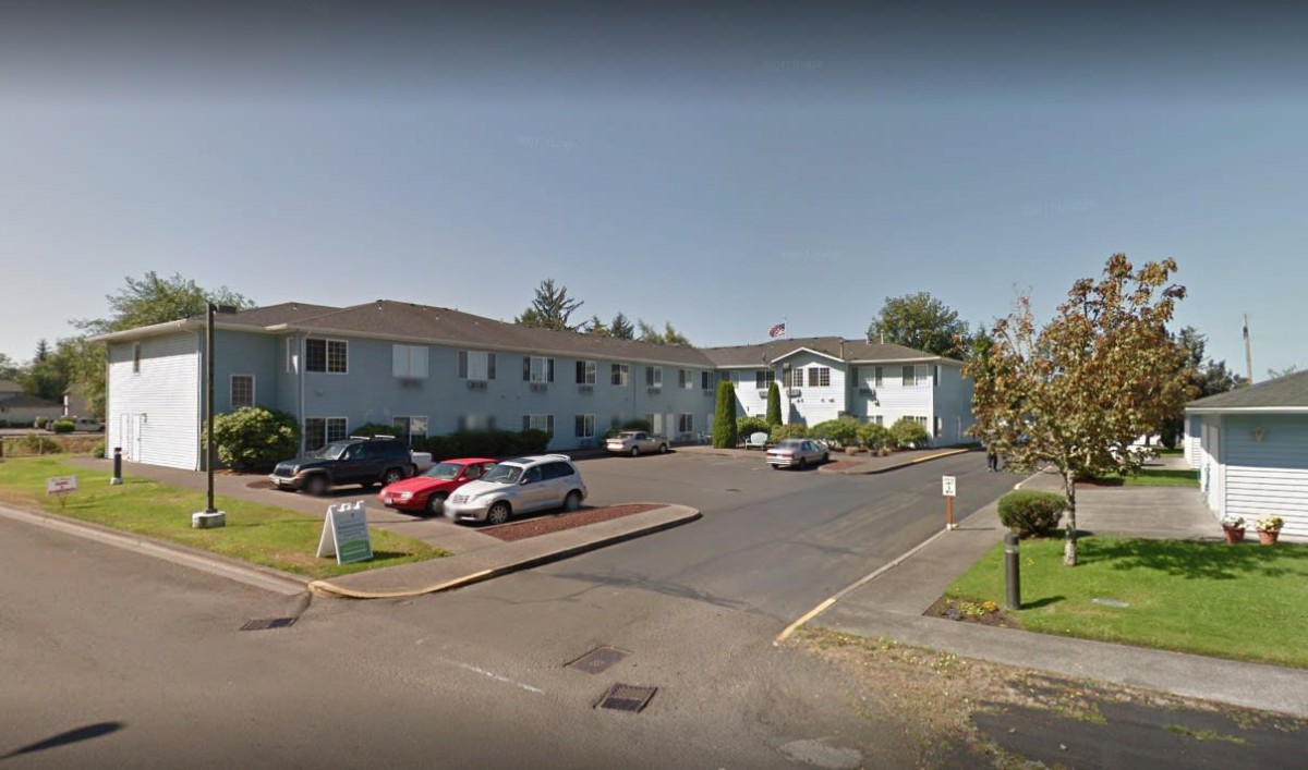 A residential apartment building with a parking lot and several parked cars.