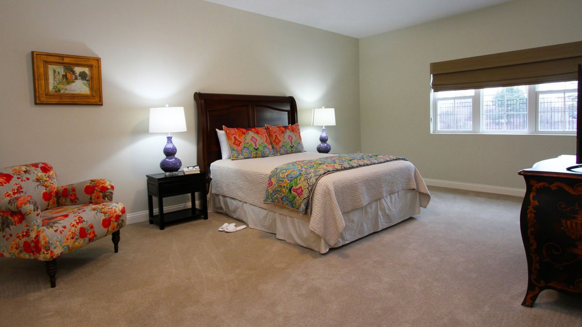 A cozy bedroom with a neatly made bed, flanked by nightstands and lamps, in soft neutral tones.