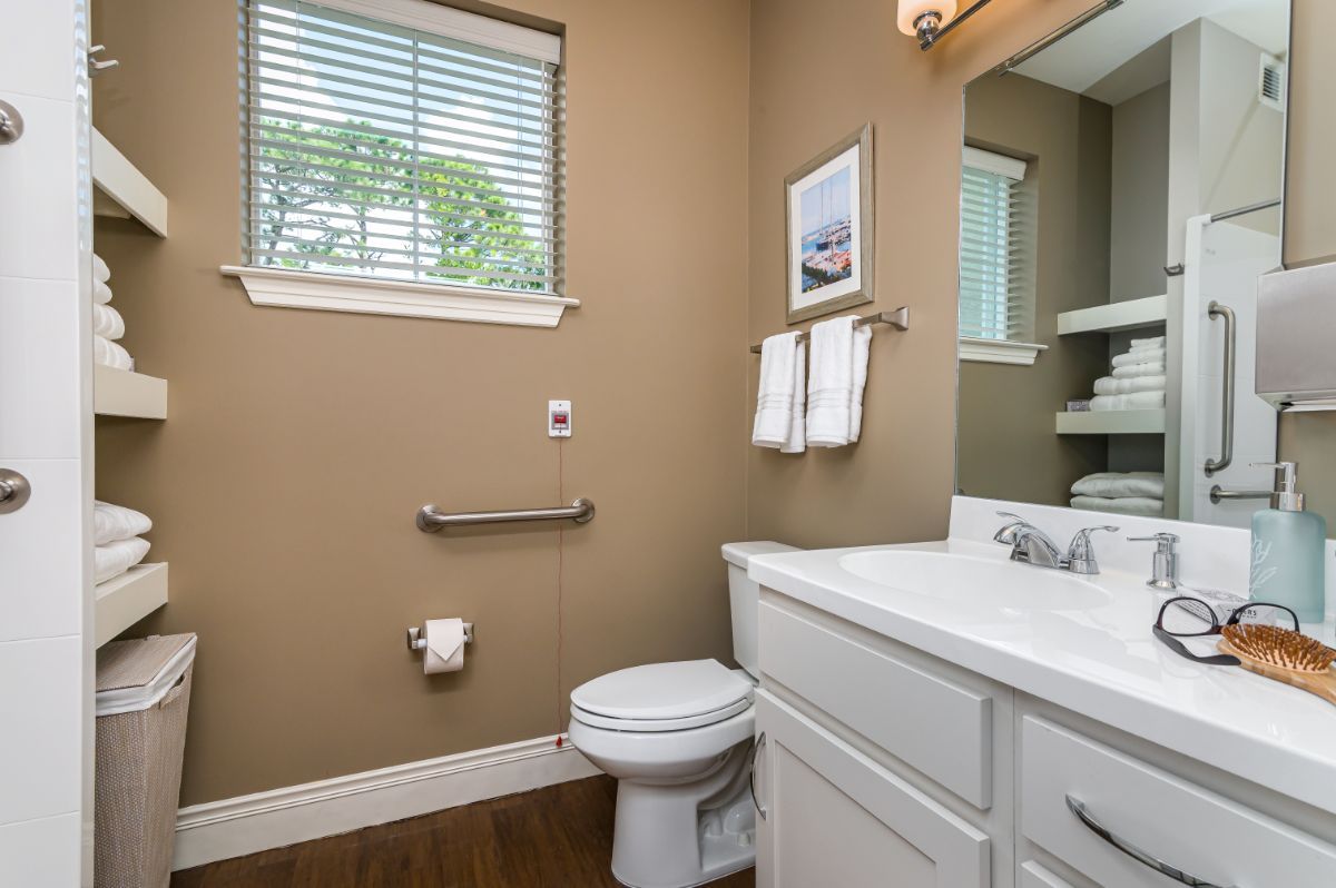 A well-lit bathroom with a toilet, sink, mirror, and window.