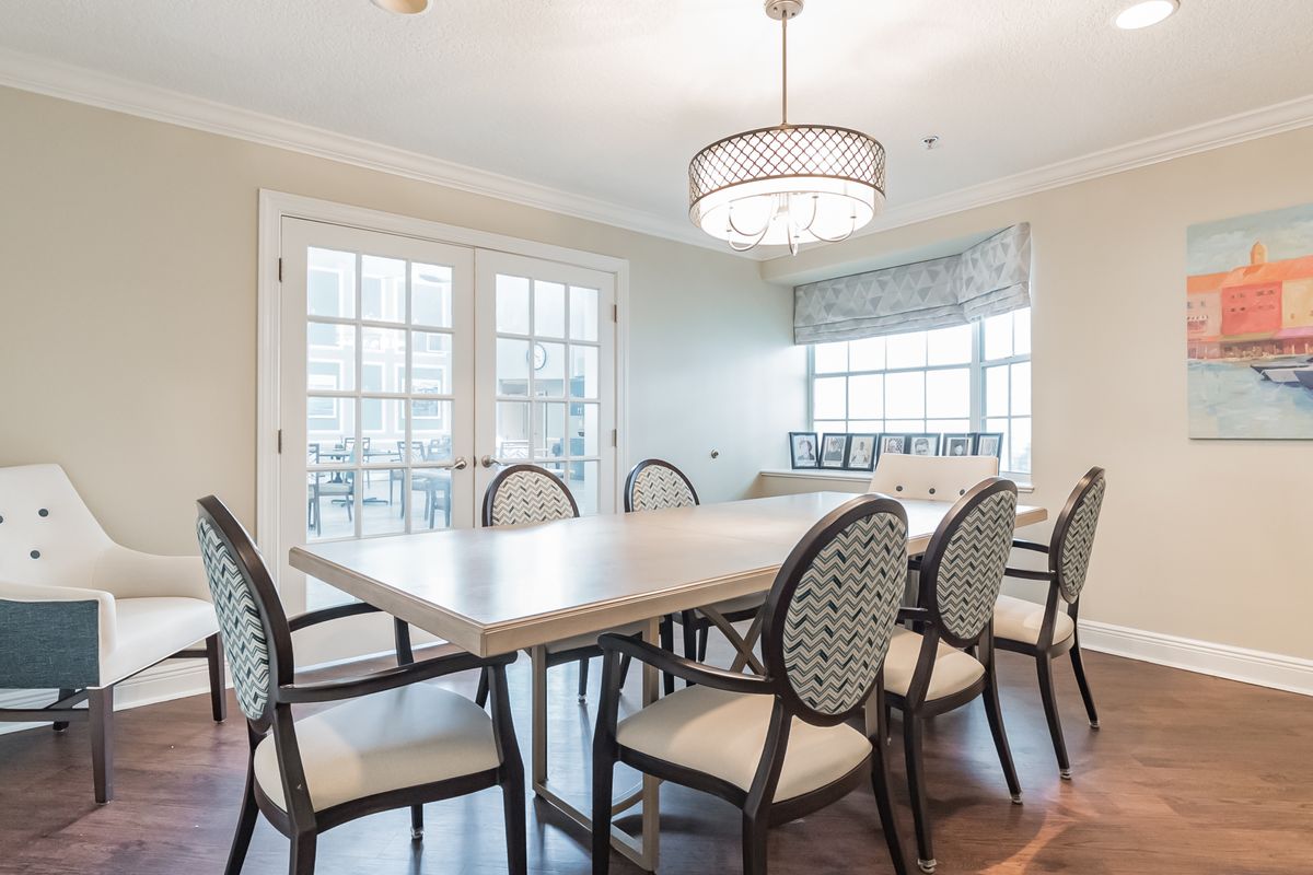A well-lit dining room featuring a large table surrounded by elegant chairs, with a modern chandelier and large windows providing natural light.