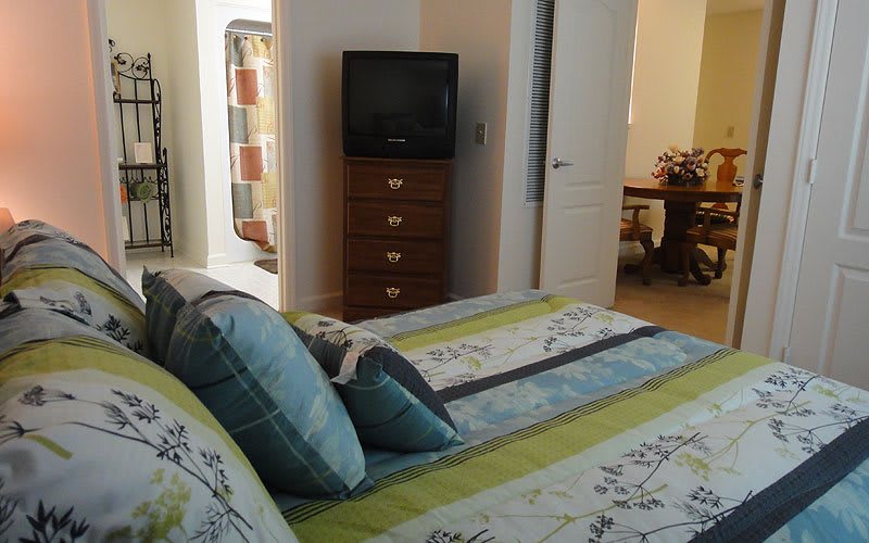 A cozy bedroom featuring a neatly made bed, a television on a dresser, and an open doorway.