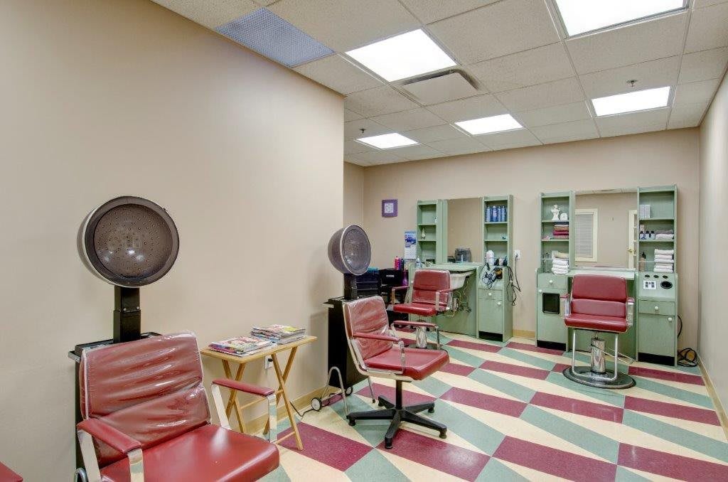 An interior view of a hair salon with retro styling chairs and hooded hair dryers on a checkered floor.