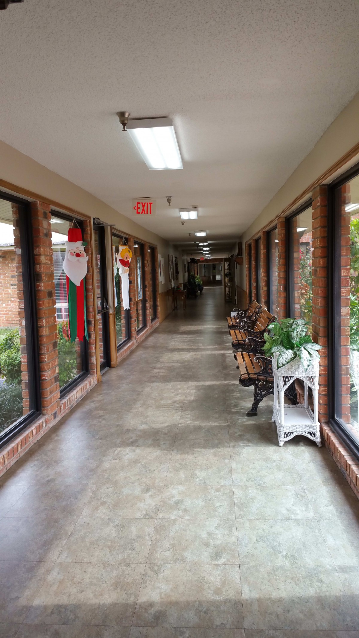A long indoor hallway with brick walls and large windows, decorated with seasonal decorations and potted plants.
