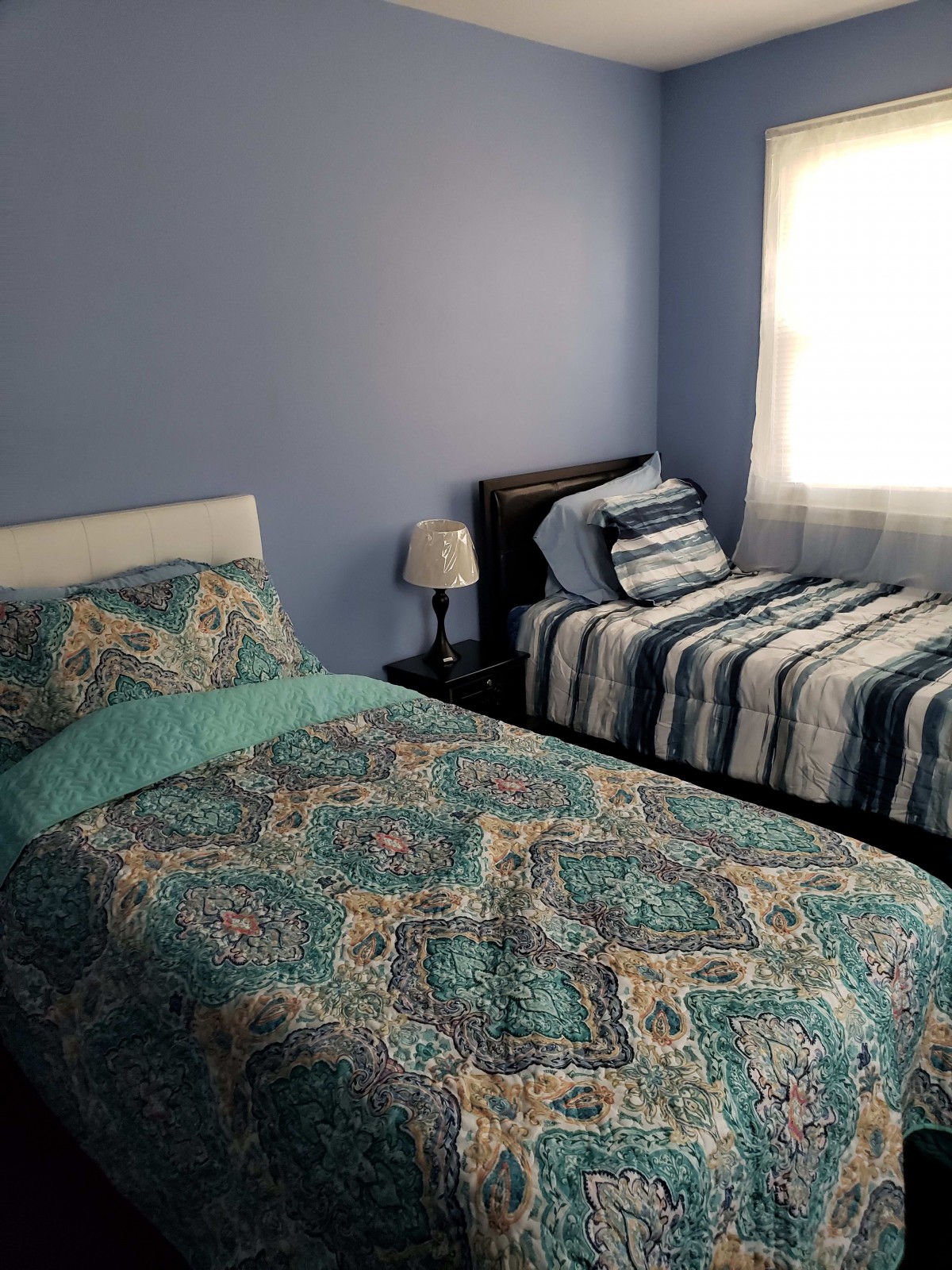 A bedroom with twin beds and blue walls, featuring patterned bedding and a bedside lamp.