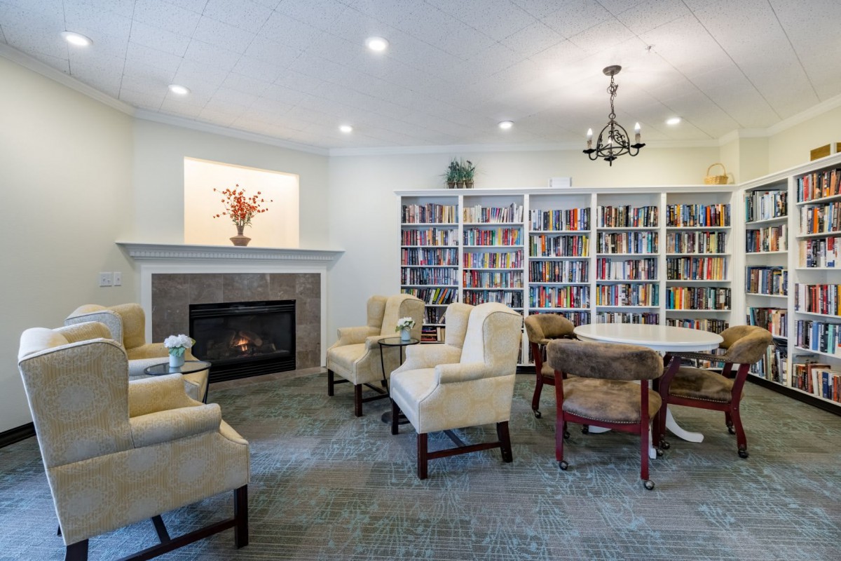 A cozy library room with bookshelves, a fireplace, and comfortable seating.