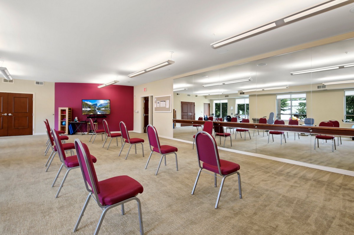An empty meeting room with red chairs arranged in a circle, featuring a mirrored wall and a television.