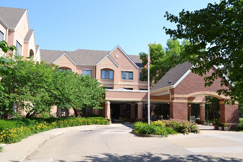 A large brick building with a main entrance surrounded by trees and a circular driveway.