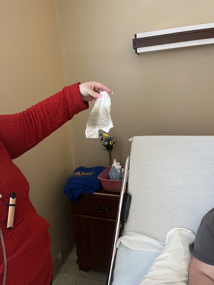 A person in red is holding a gown next to a hospital bed.