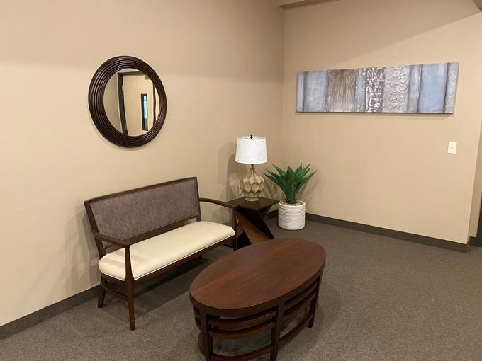 A cozy waiting room with a sofa, oval table, lamp, and decorative elements.