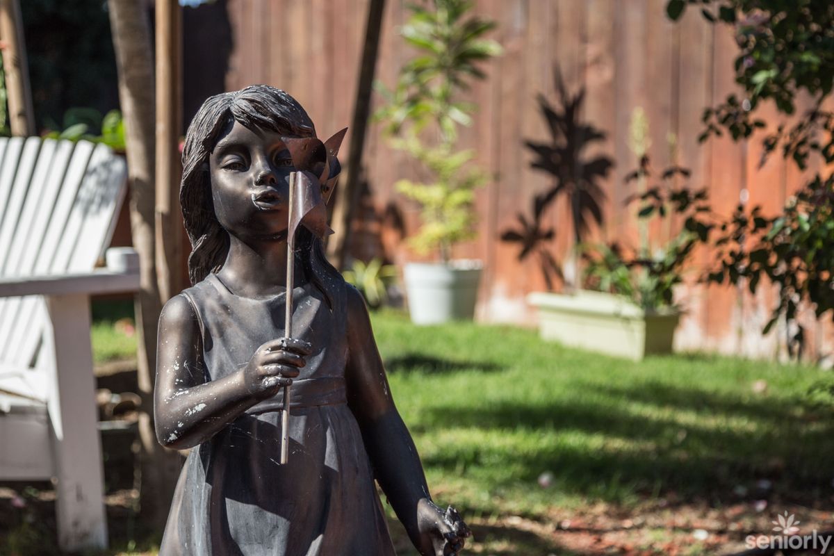 A garden sculpture of a girl holding a flower under sunlight.