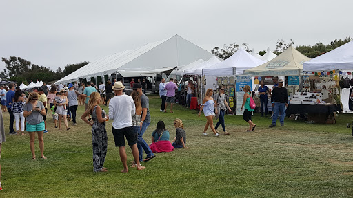 A lively outdoor festival featuring various tents and people enjoying the event.