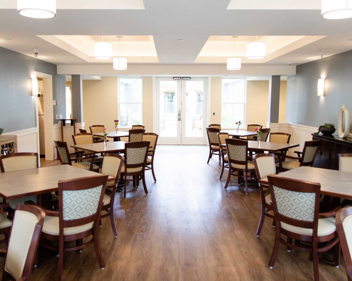 An elegant dining room with multiple tables and chairs, featuring wood flooring and soft lighting.