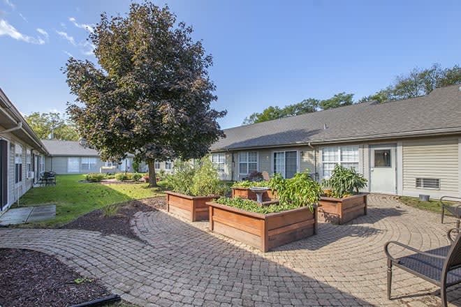 A courtyard featuring raised garden beds filled with plants, surrounded by a paved pathway.