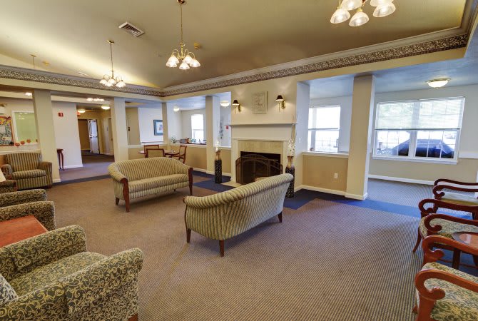 A cozy living room with sofas surrounding a fireplace and large windows letting in natural light.