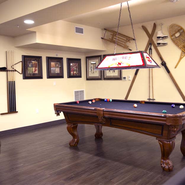 A stylish game room featuring a classic pool table with wall decorations and sleek wooden flooring.