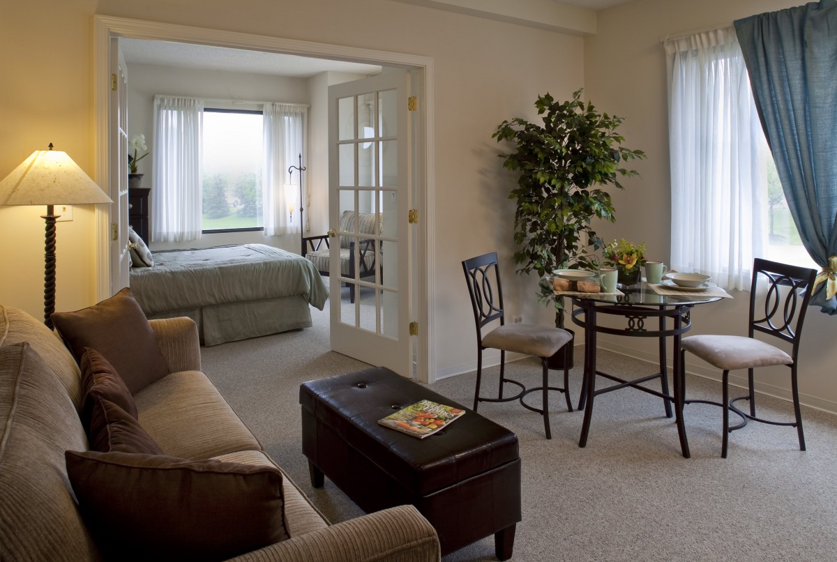 A cozy apartment interior featuring a living area and a bedroom with natural light.
