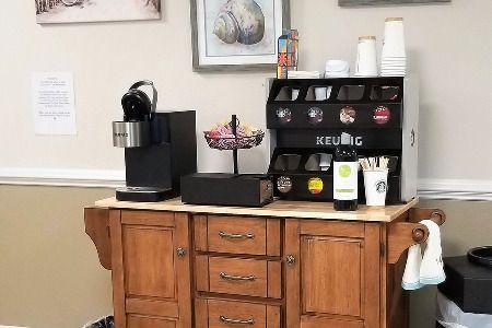 A cozy coffee station with a coffee maker, variety of coffee pods, and creamers on a wooden cabinet.