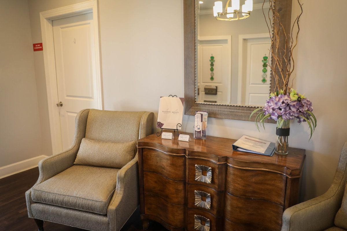 A cozy office waiting area featuring a comfortable armchair and a wooden desk with decorative items, accompanied by a large mirror.