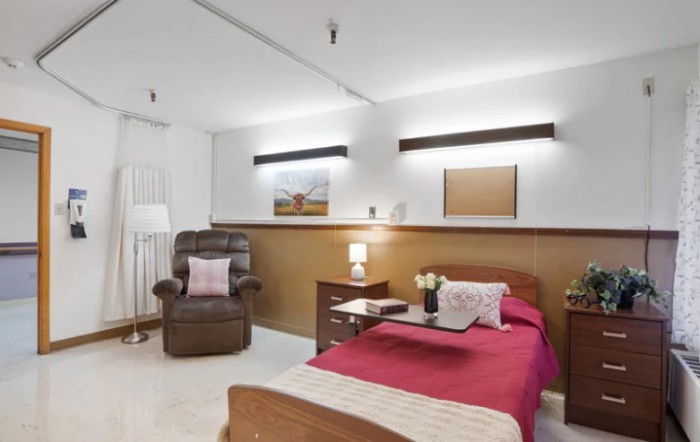 A cozy bedroom featuring a comfortable bed with red bedding, a bedside table with a lamp, and an armchair in the corner.