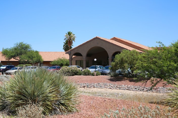 A desert-style building with a red-tiled roof surrounded by arid landscaping under a clear blue sky.