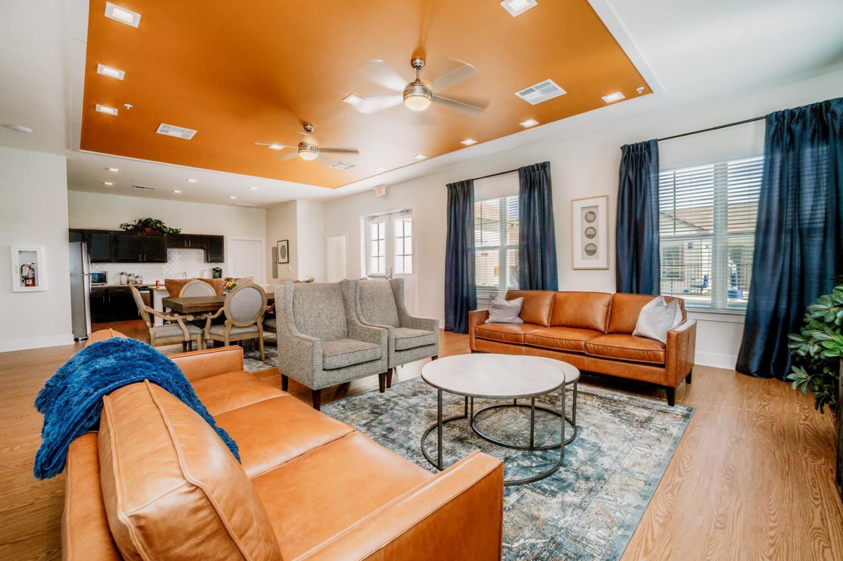 A modern living room with orange ceiling, leather sofas, and blue curtains.