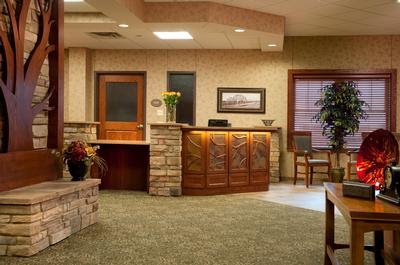 A cozy and welcoming reception area featuring wooden furnishings, a green carpet, and decorative plants.