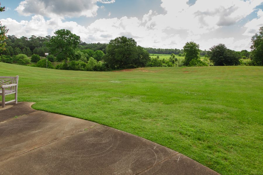 A scenic view of a lush green lawn bordered by trees under a partly cloudy sky.