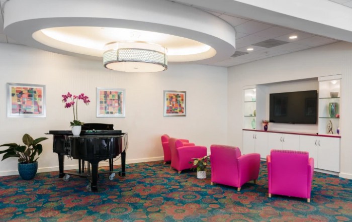 A modern lobby with pink chairs, a grand piano, and colorful artwork.