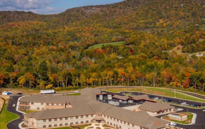 Aerial view of a building surrounded by vibrant autumn foliage and mountains.