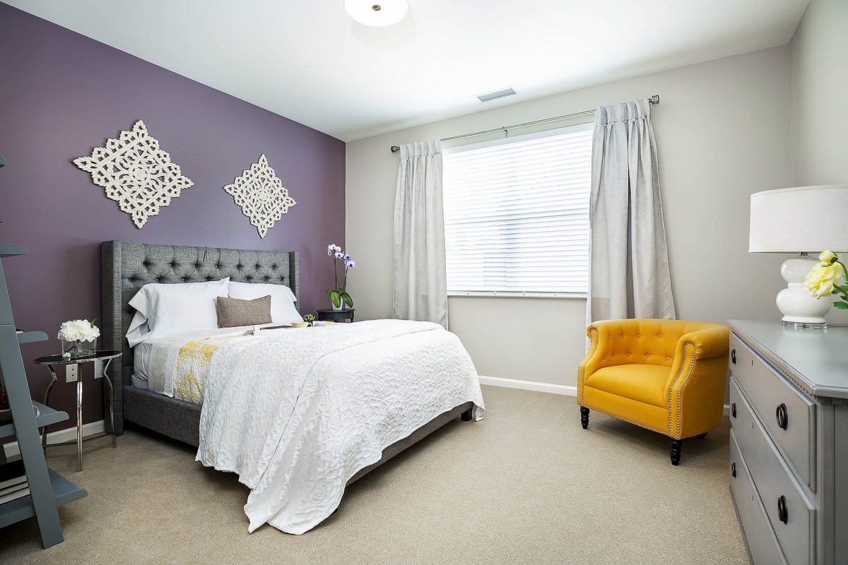 A modern bedroom with a purple accent wall, featuring a comfortable bed and a bright yellow chair.